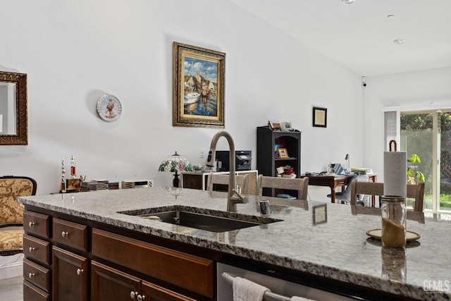 kitchen featuring light stone counters, wood finished floors, a sink, dark brown cabinets, and stainless steel dishwasher