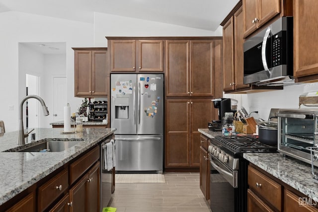 kitchen featuring lofted ceiling, light stone counters, stainless steel appliances, light wood-style floors, and a sink