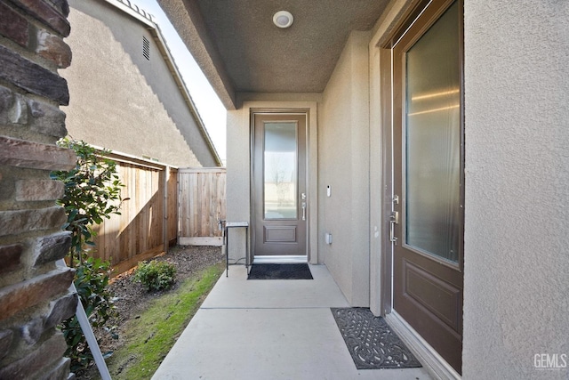 view of exterior entry featuring fence and stucco siding