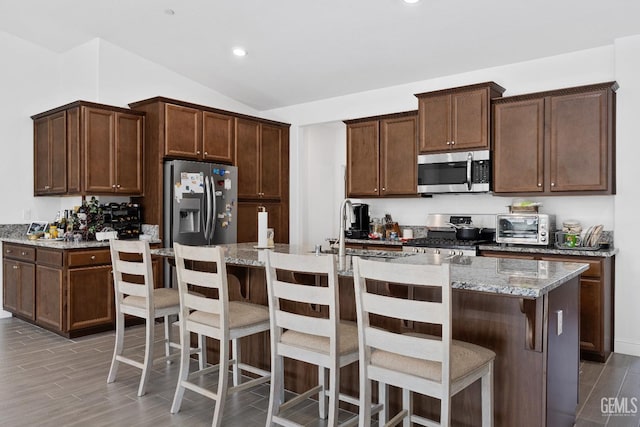 kitchen featuring a breakfast bar, light stone countertops, a kitchen island with sink, and stainless steel appliances