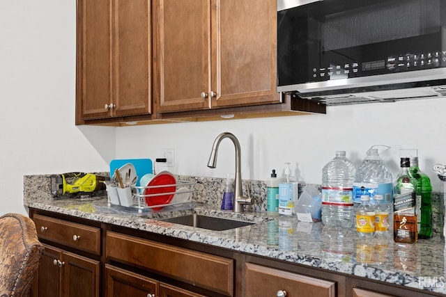 kitchen featuring light stone countertops, stainless steel microwave, brown cabinetry, and a sink