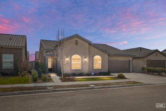 mediterranean / spanish house with driveway, a tiled roof, a garage, and stucco siding