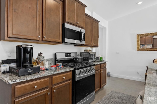 kitchen featuring light wood-style flooring, a toaster, stainless steel appliances, baseboards, and light stone countertops