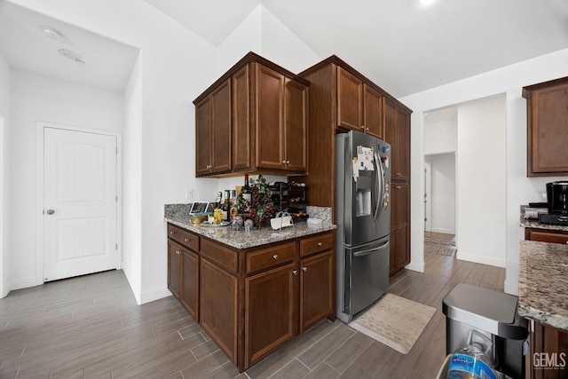 kitchen with baseboards, light stone counters, wood finished floors, and stainless steel fridge with ice dispenser