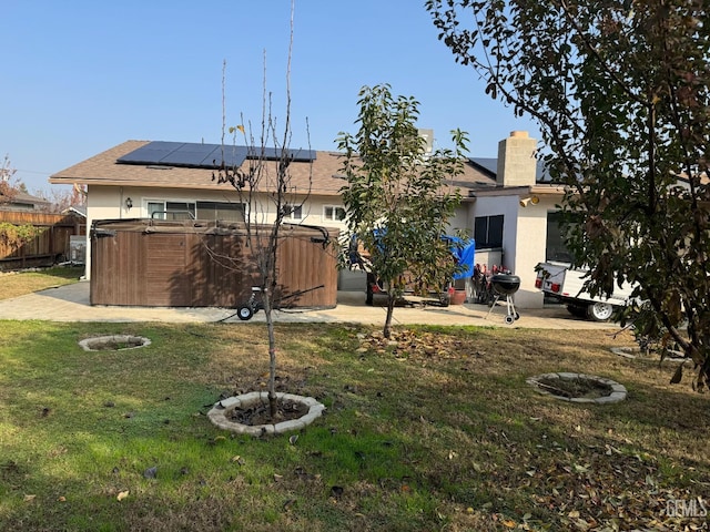 rear view of house with solar panels, a yard, and a hot tub