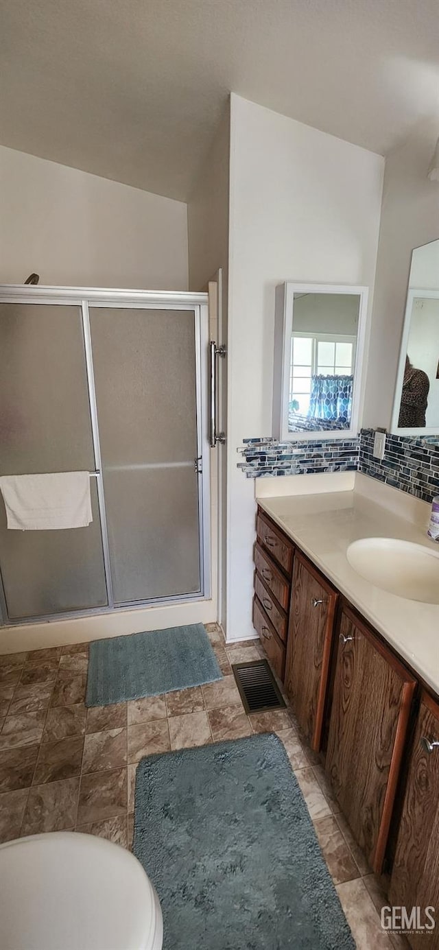 bathroom featuring vanity, tasteful backsplash, toilet, and a shower with shower door