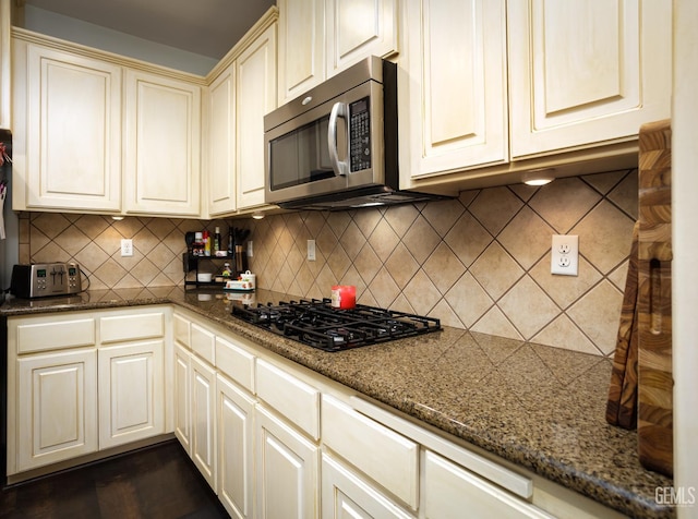 9900 Swansboro Way, Bakersfield, CA 93314 - kitchen with stainless steel microwave, black gas cooktop, cream cabinetry, decorative backsplash, and dark stone counters