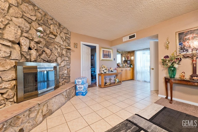 living room featuring light tile patterned floors, a stone fireplace, a textured ceiling, and visible vents