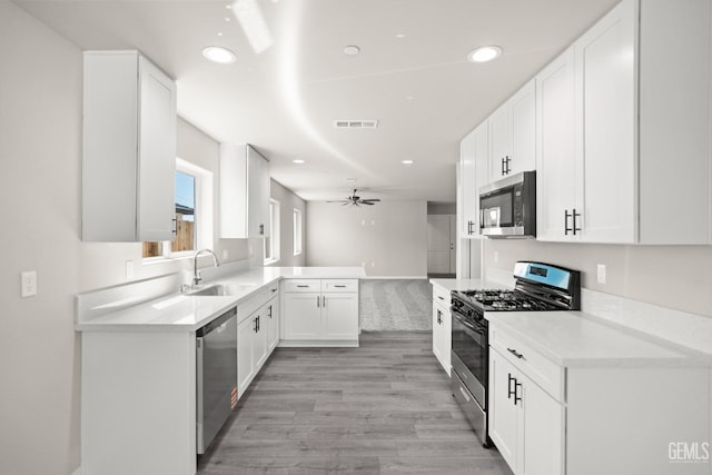 707 Poinsettia St, Bakersfield, CA 93307 - kitchen with stainless steel appliances, a sink, light wood-style floors, white cabinets, and a ceiling fan