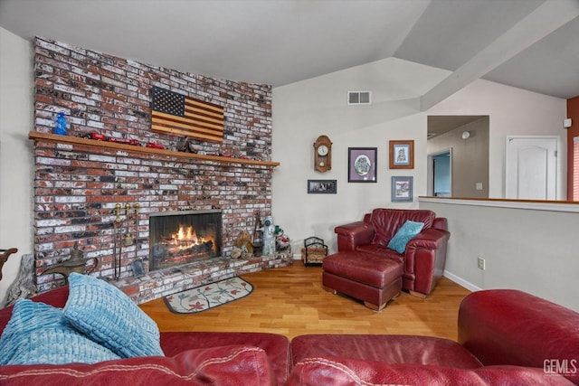 living area with a brick fireplace, visible vents, vaulted ceiling, and wood finished floors