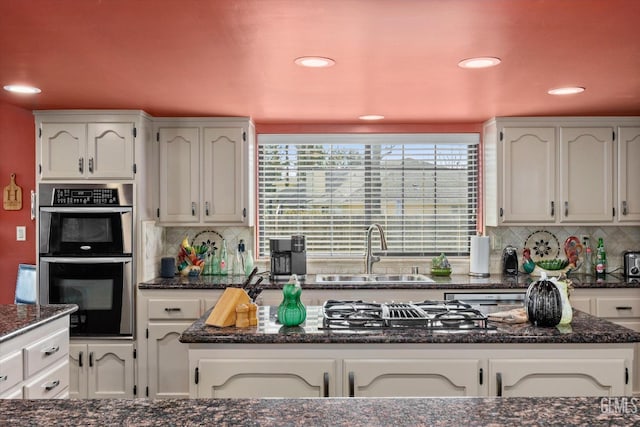 kitchen featuring double oven, recessed lighting, a sink, tasteful backsplash, and dark stone countertops