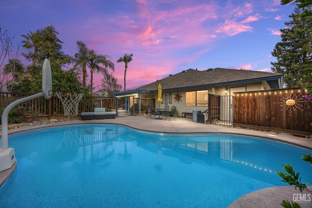 pool at dusk with a patio, an outdoor living space, fence, and a fenced in pool