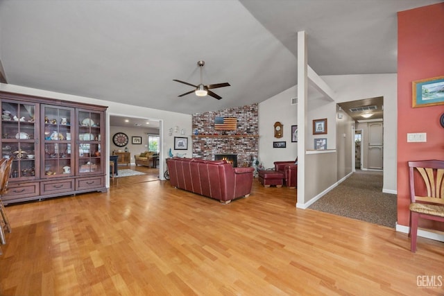 living area featuring a fireplace, light wood finished floors, vaulted ceiling, ceiling fan, and baseboards