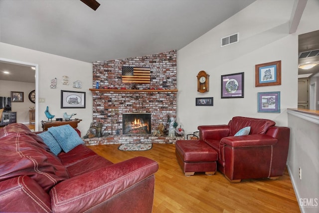 living area featuring vaulted ceiling, a fireplace, wood finished floors, and visible vents