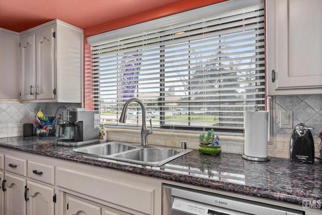 kitchen with backsplash, white cabinets, a sink, dark stone counters, and dishwashing machine