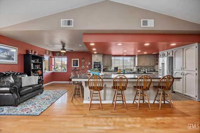 kitchen with stainless steel appliances, light wood finished floors, a kitchen bar, and visible vents