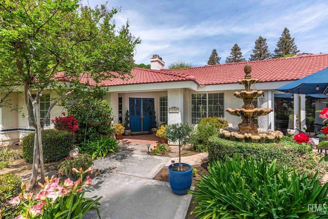 rear view of property with a chimney, stucco siding, and a tiled roof
