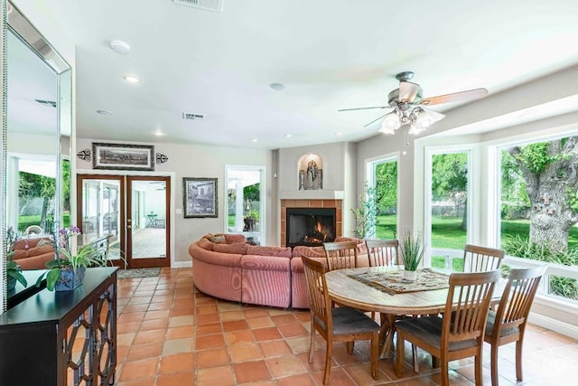 interior space featuring a ceiling fan, visible vents, a tiled fireplace, and plenty of natural light