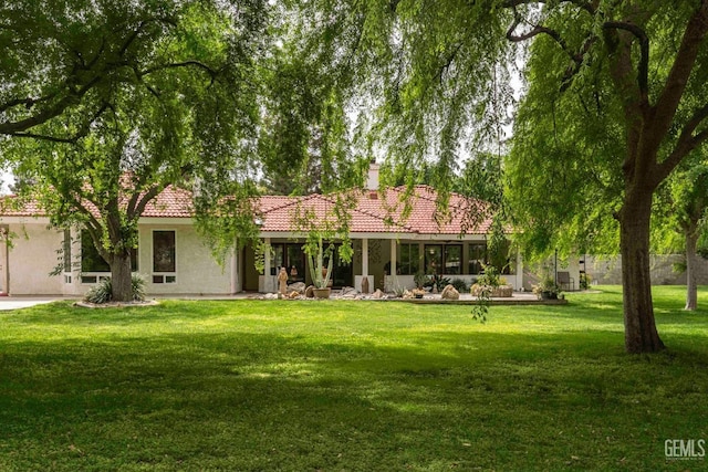 view of front facade with a chimney, stucco siding, a front yard, and a tiled roof