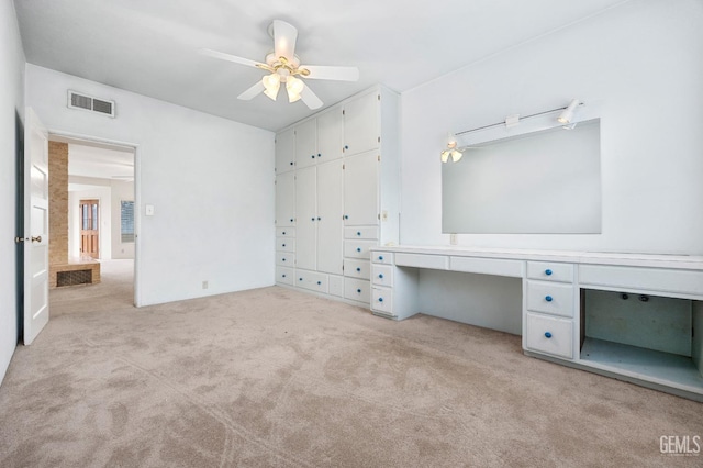 unfurnished bedroom with light carpet, built in desk, a closet, and ceiling fan