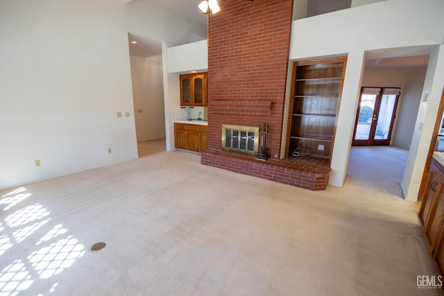 unfurnished living room featuring french doors, light colored carpet, a towering ceiling, and a fireplace