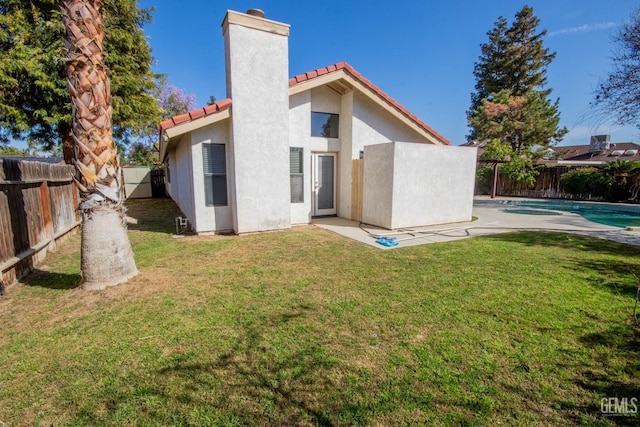 back of house with stucco siding, a tile roof, a fenced backyard, a yard, and a chimney