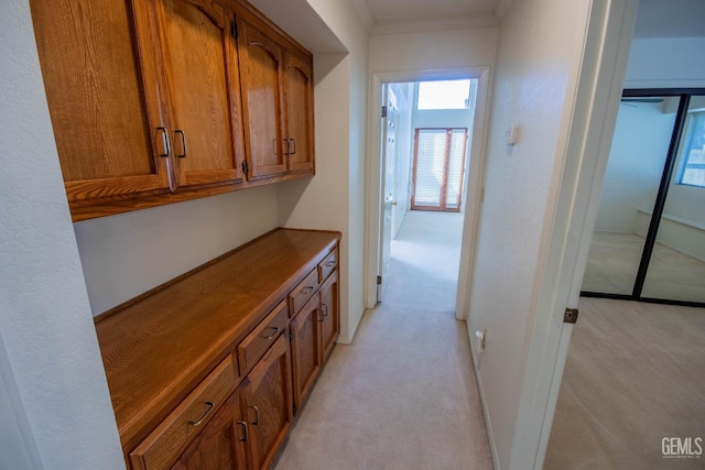 hallway with light carpet, crown molding, and baseboards