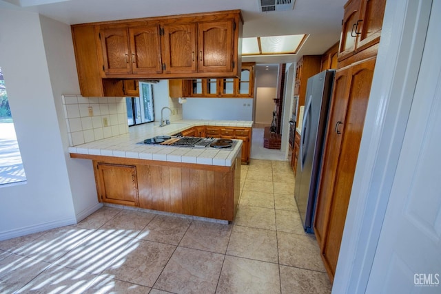 kitchen featuring freestanding refrigerator, stovetop, a peninsula, brown cabinetry, and decorative backsplash