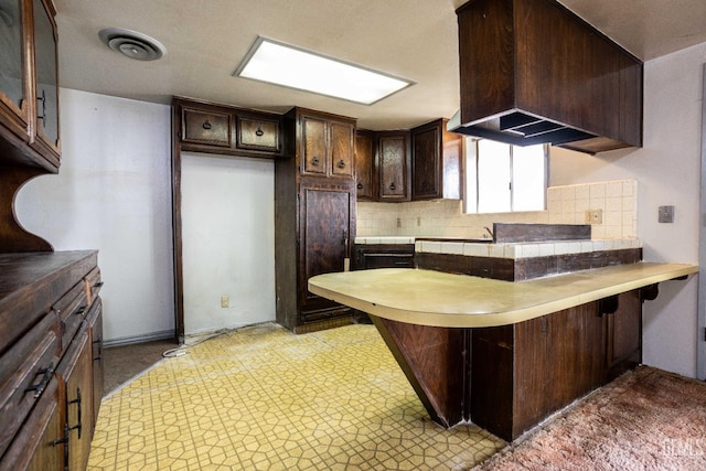 kitchen featuring tasteful backsplash, dark brown cabinets, a kitchen breakfast bar, and kitchen peninsula