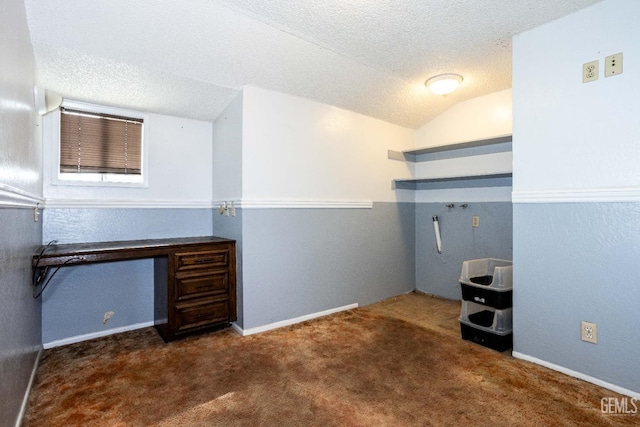 unfurnished office featuring dark carpet, vaulted ceiling, and a textured ceiling