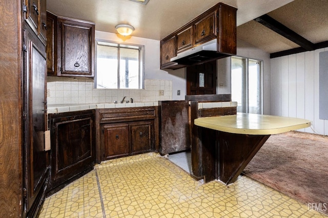 kitchen with dark brown cabinetry, sink, tasteful backsplash, wooden walls, and beam ceiling