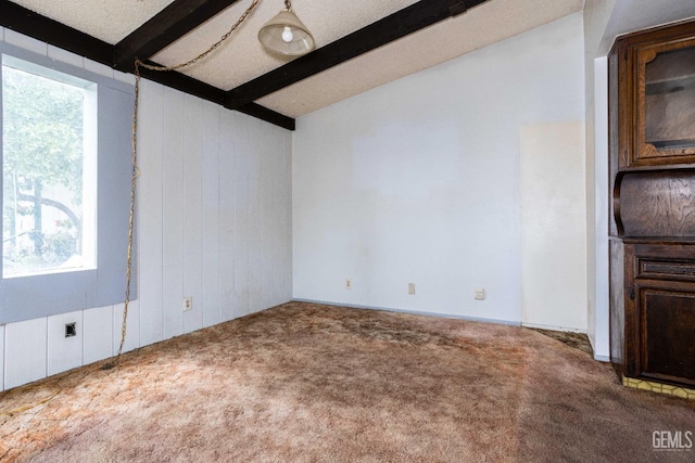 carpeted empty room featuring wooden walls, lofted ceiling with beams, and a textured ceiling