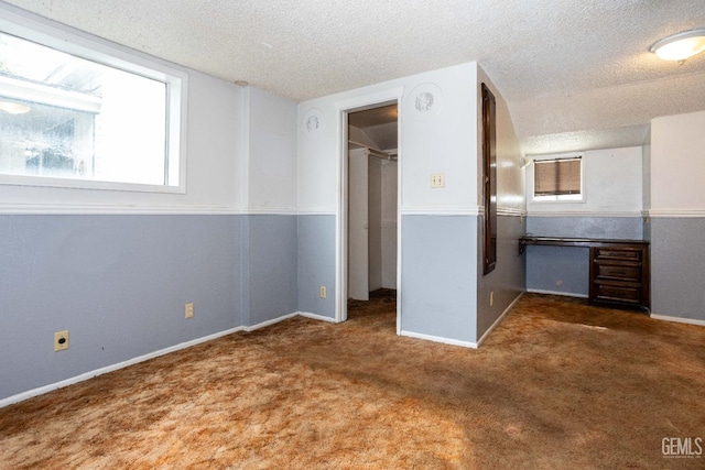 unfurnished bedroom featuring dark carpet, a walk in closet, and a textured ceiling