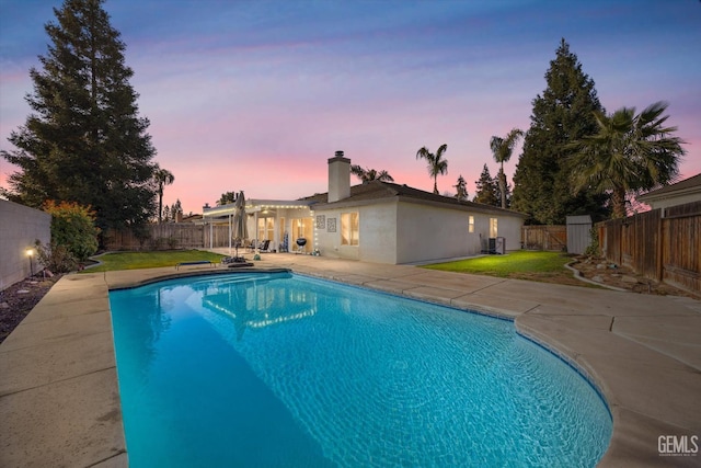 pool at dusk with cooling unit, a yard, and a patio area