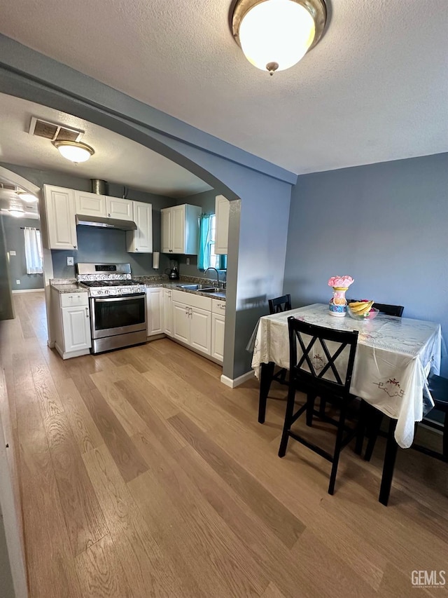 kitchen with white cabinetry, sink, light hardwood / wood-style floors, stainless steel gas range oven, and a textured ceiling