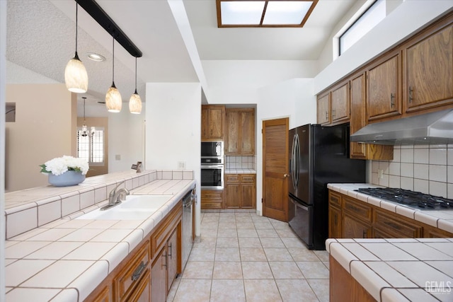 9408 Wandering Oak Dr, Bakersfield, CA 93311 - kitchen with tile counters, under cabinet range hood, stainless steel appliances, a sink, and brown cabinets