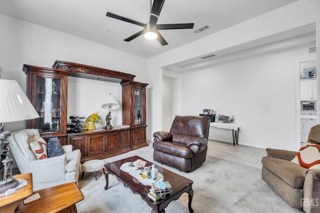 living area with light colored carpet, visible vents, a ceiling fan, and washer / clothes dryer