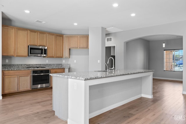 6522 Bangor Pl, Bakersfield, CA 93313 - kitchen featuring stainless steel appliances, light wood-style flooring, arched walkways, light stone countertops, and a kitchen island with sink