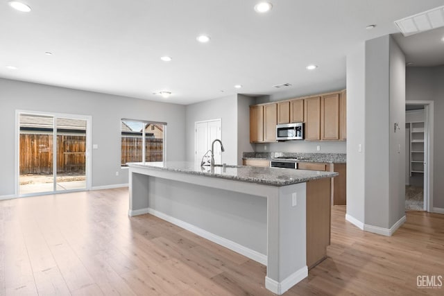 6522 Bangor Pl, Bakersfield, CA 93313 - kitchen with stainless steel microwave, light wood-type flooring, a kitchen island with sink, recessed lighting, and light stone counters
