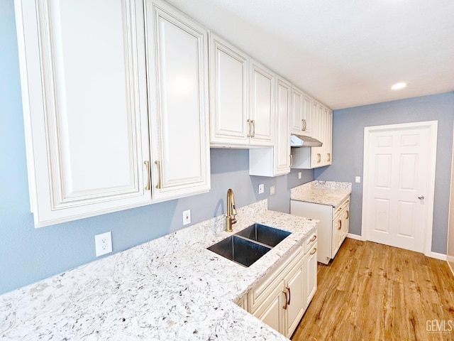 kitchen featuring light stone countertops, sink, white cabinets, and light hardwood / wood-style flooring