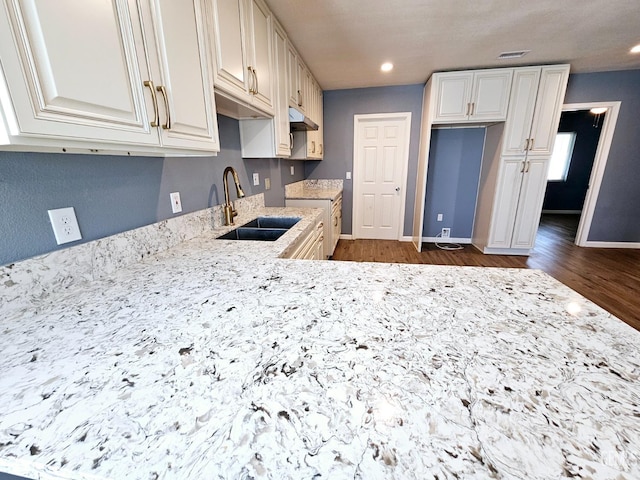 kitchen with white cabinets, light stone countertops, sink, and dark wood-type flooring