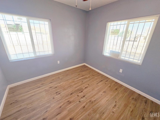 spare room with light wood-type flooring, ceiling fan, and a healthy amount of sunlight