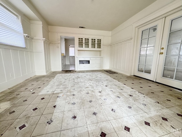 unfurnished living room with visible vents, a fireplace, french doors, and a decorative wall