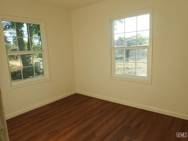 spare room featuring baseboards, dark wood-type flooring, and plenty of natural light