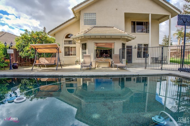 rear view of house with stucco siding, fence, a patio area, a fenced in pool, and a tiled roof