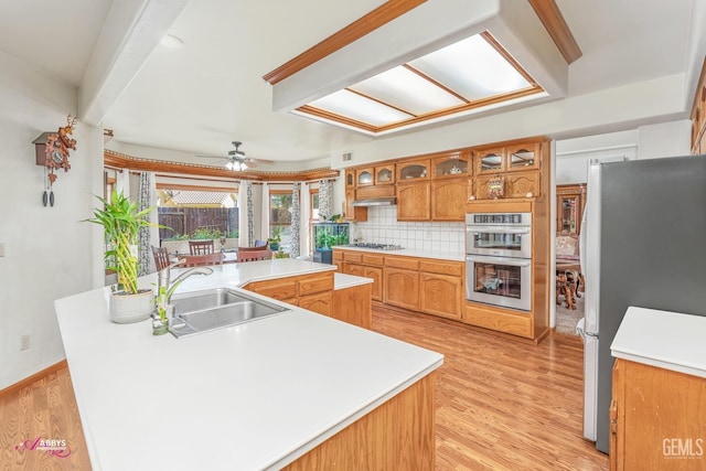 kitchen with a sink, stainless steel appliances, light wood-type flooring, and backsplash