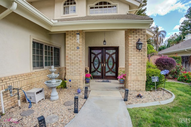 entrance to property with stucco siding, fence, brick siding, and french doors