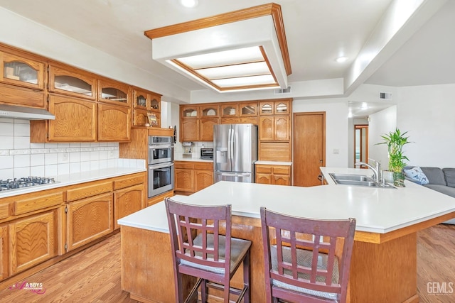 kitchen with brown cabinetry, visible vents, light wood-style flooring, a sink, and appliances with stainless steel finishes