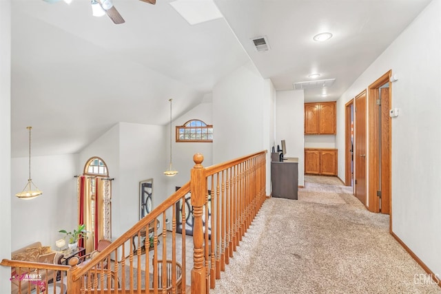 hall with visible vents, baseboards, an upstairs landing, vaulted ceiling, and light colored carpet