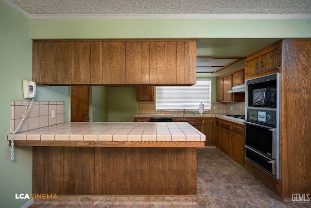 kitchen featuring backsplash, tile counters, black appliances, and kitchen peninsula